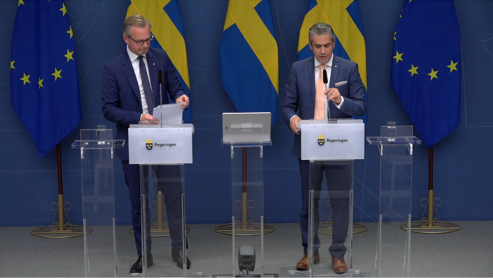 Ministrarna talar under pressträffen framför svenska flaggor